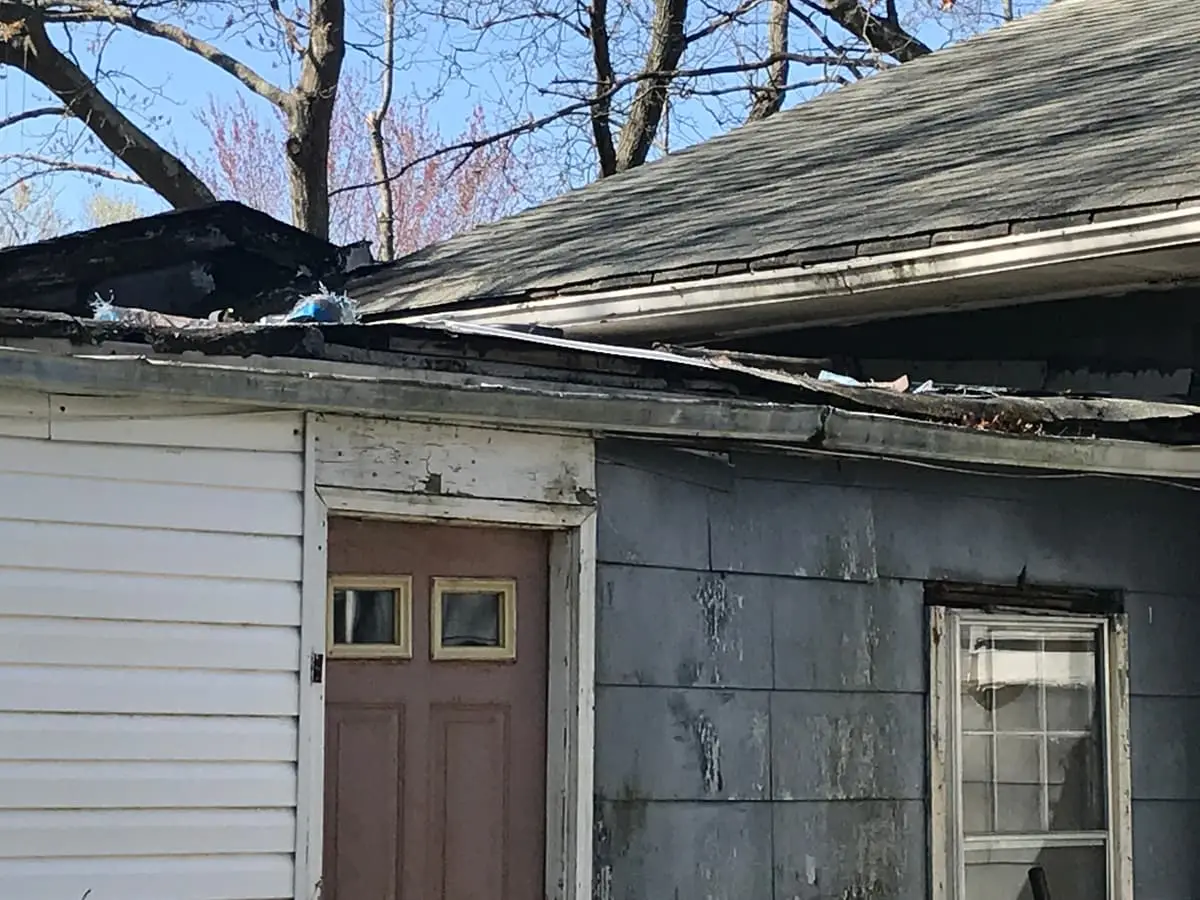 Selling a storm-damaged house in Mastic: damaged roof edge above a weathered back door
