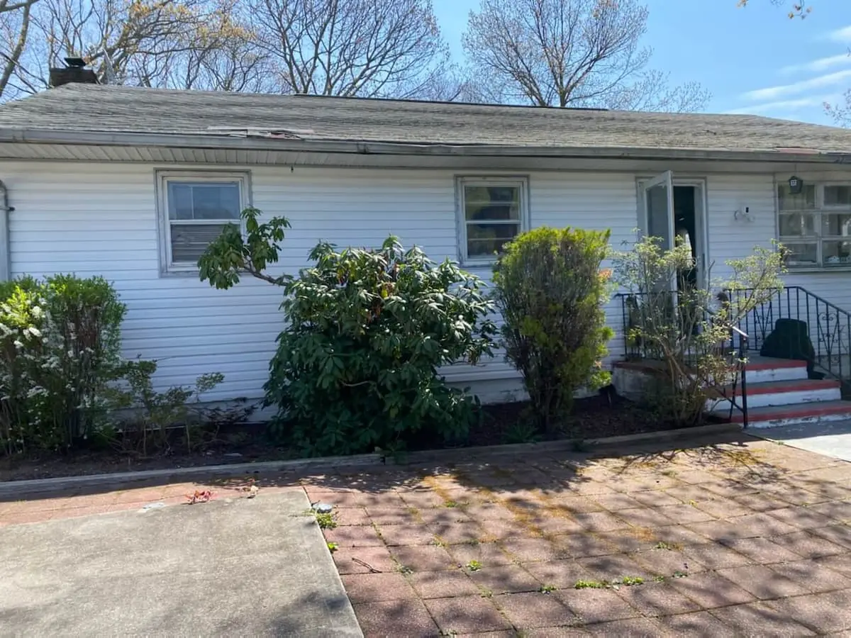 Selling a rental property in Mastic: white ranch with tall shrubs along the front